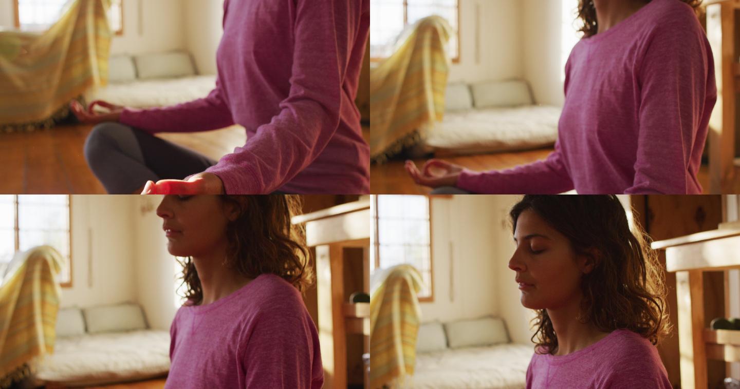轻松的混血女子练习瑜伽，坐在阳光明媚的小屋卧室冥想