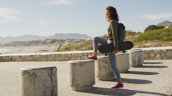 抱着滑板的混血女子停在海边欣赏风景