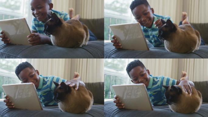 快乐的非洲裔美国男孩坐在沙发上看书和微笑，宠物猫坐在前景