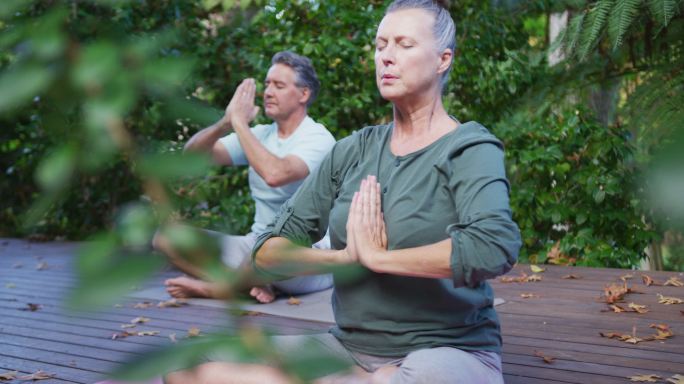 轻松的资深白人夫妇快乐地练习瑜伽，坐在花园里冥想