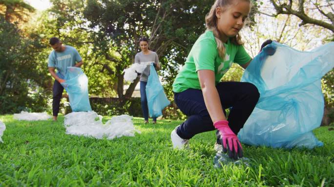 微笑的白人女儿拿着垃圾袋，和父母一起收集塑料垃圾