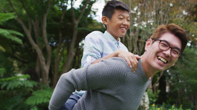微笑的亚洲父亲猪背快乐的儿子在花园里玩在一起