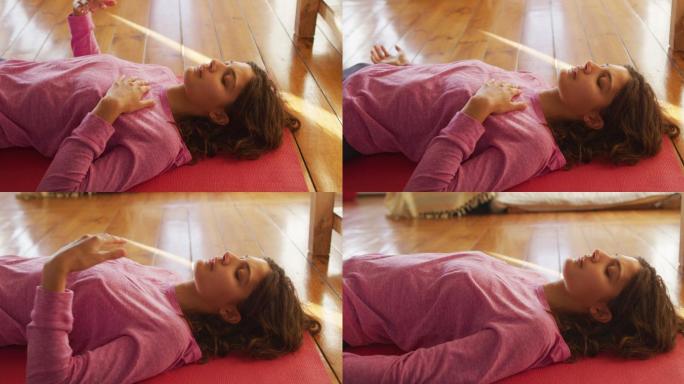 轻松的混血儿女人练习瑜伽，躺在垫子上闭着眼睛在阳光明媚的小屋卧室