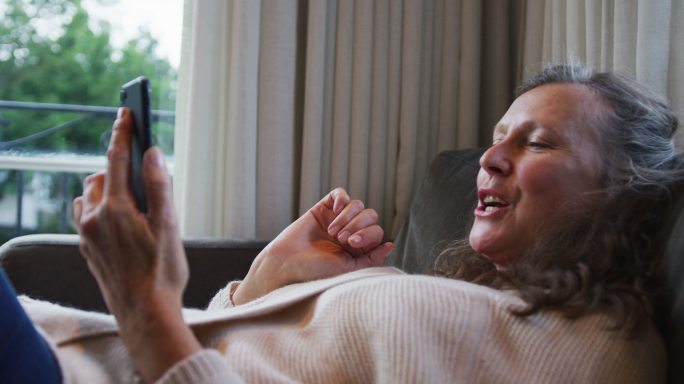 快乐的白人妇女放松和视频通话使用智能手机，交谈和微笑
