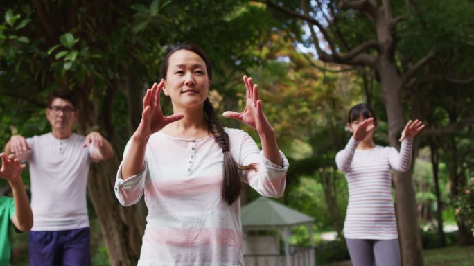 快乐的亚洲父母与儿子和女儿在花园里锻炼，一起练习太极