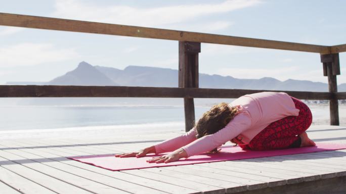 健康的混血女子在户外练习瑜伽，跪在海边，伸展身体