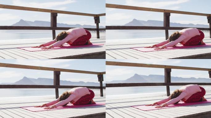 健康的混血女子在户外练习瑜伽，跪在海边，伸展身体