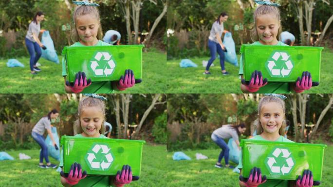 微笑的白人女儿在户外拿着回收箱，和父母一起收集塑料垃圾