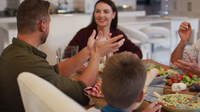 微笑的白人父母和祖父在餐桌上和孙子聊天