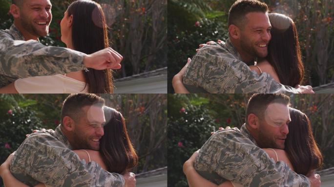 微笑的白人男性士兵拥抱他幸福的妻子在花园外的房子