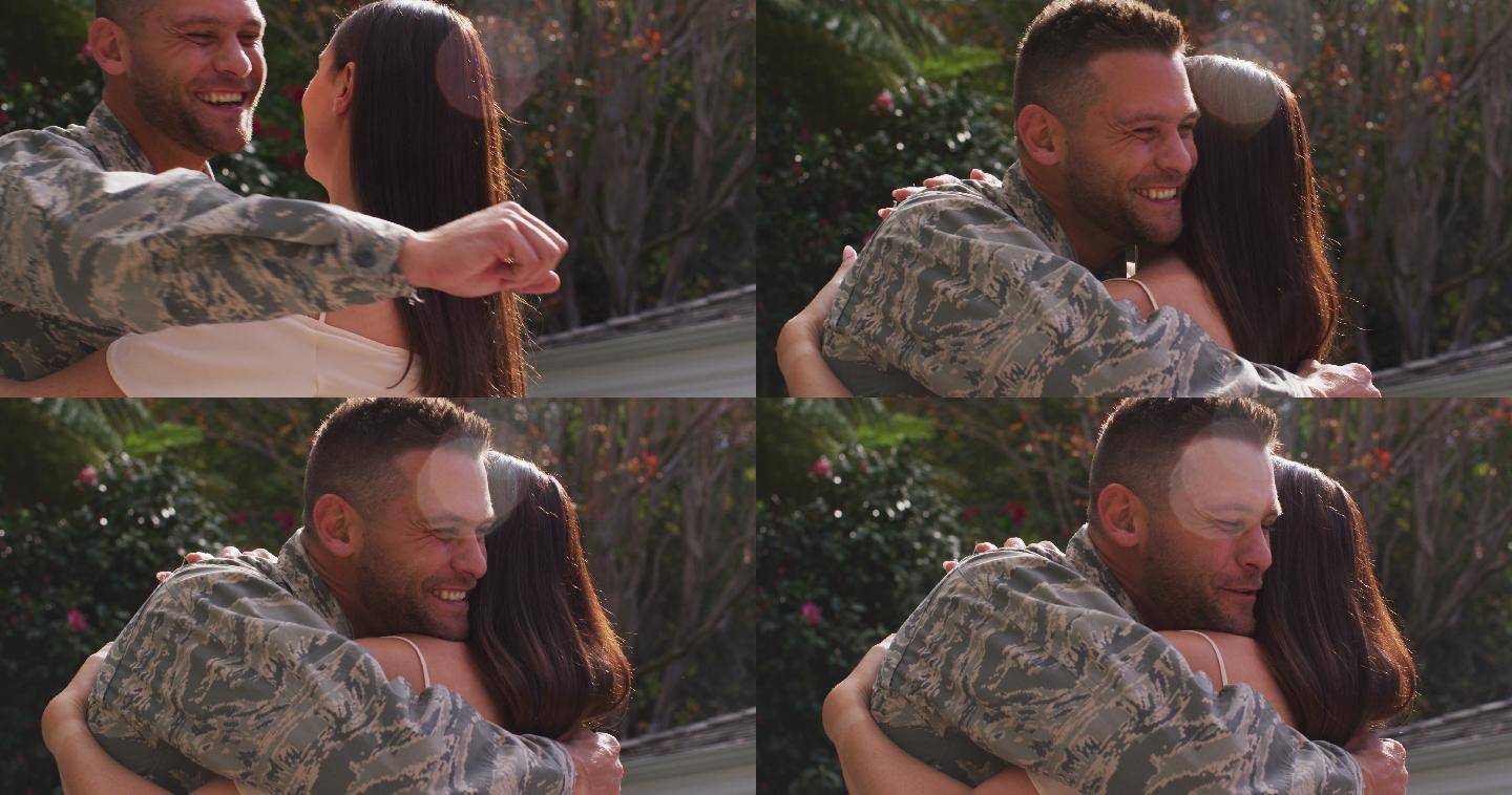 微笑的白人男性士兵拥抱他幸福的妻子在花园外的房子