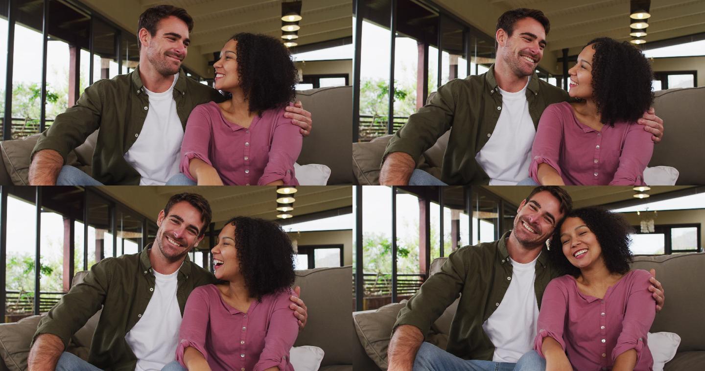 一对混血儿夫妇坐在度假屋的沙发上，面带微笑地看着对方