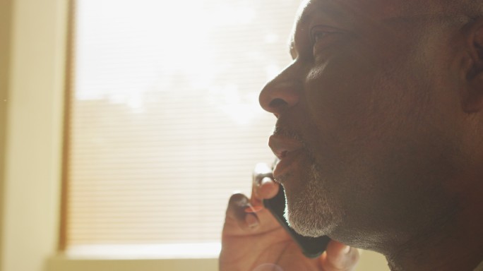 一位深思熟虑的非裔美国老人坐在家里晒太阳，用智能手机聊天
