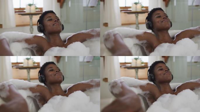 微笑的非洲裔美国人有吸引力的女人戴着耳机放松在泡沫浴在浴室