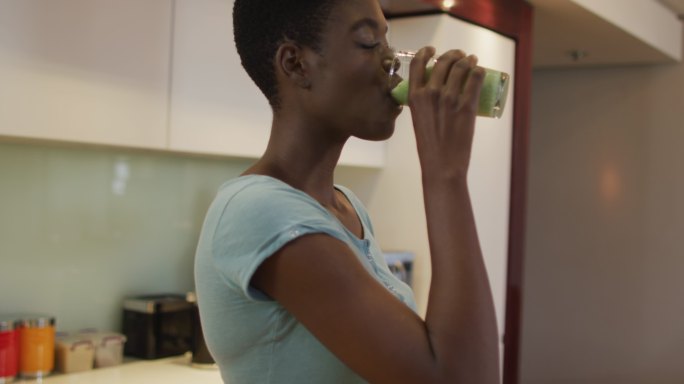 微笑的非洲裔美国人迷人的女人在厨房喝自制冰沙的简介