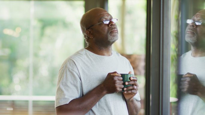 一个深思熟虑的非洲裔美国老人站在那里喝着咖啡，看着窗外