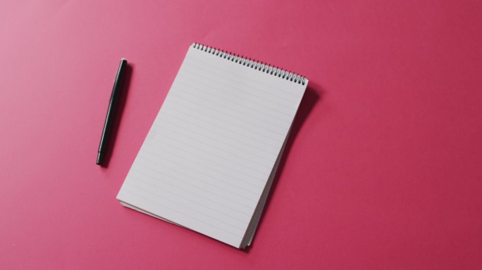 钢笔和笔记本的视频与复制空间在粉红色的背景