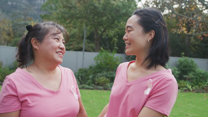 快乐的亚洲母亲在花园拥抱成年的女儿，穿着粉红色的t恤