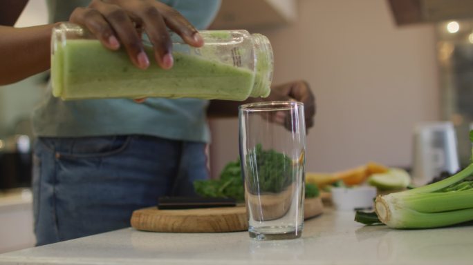 非裔美国美女的手在厨房里把自制的冰沙倒进玻璃杯里