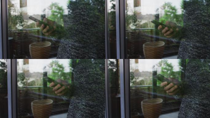 一名男子使用智能手机，透过家里的窗户看到，带有反射
