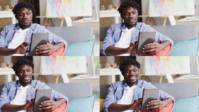 非裔美国男艺术家微笑着坐在艺术工作室的沙发上使用数码平板电脑