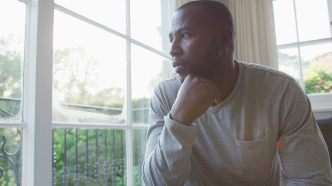 一个紧张的非裔美国人坐在家里的沙发上看着窗外