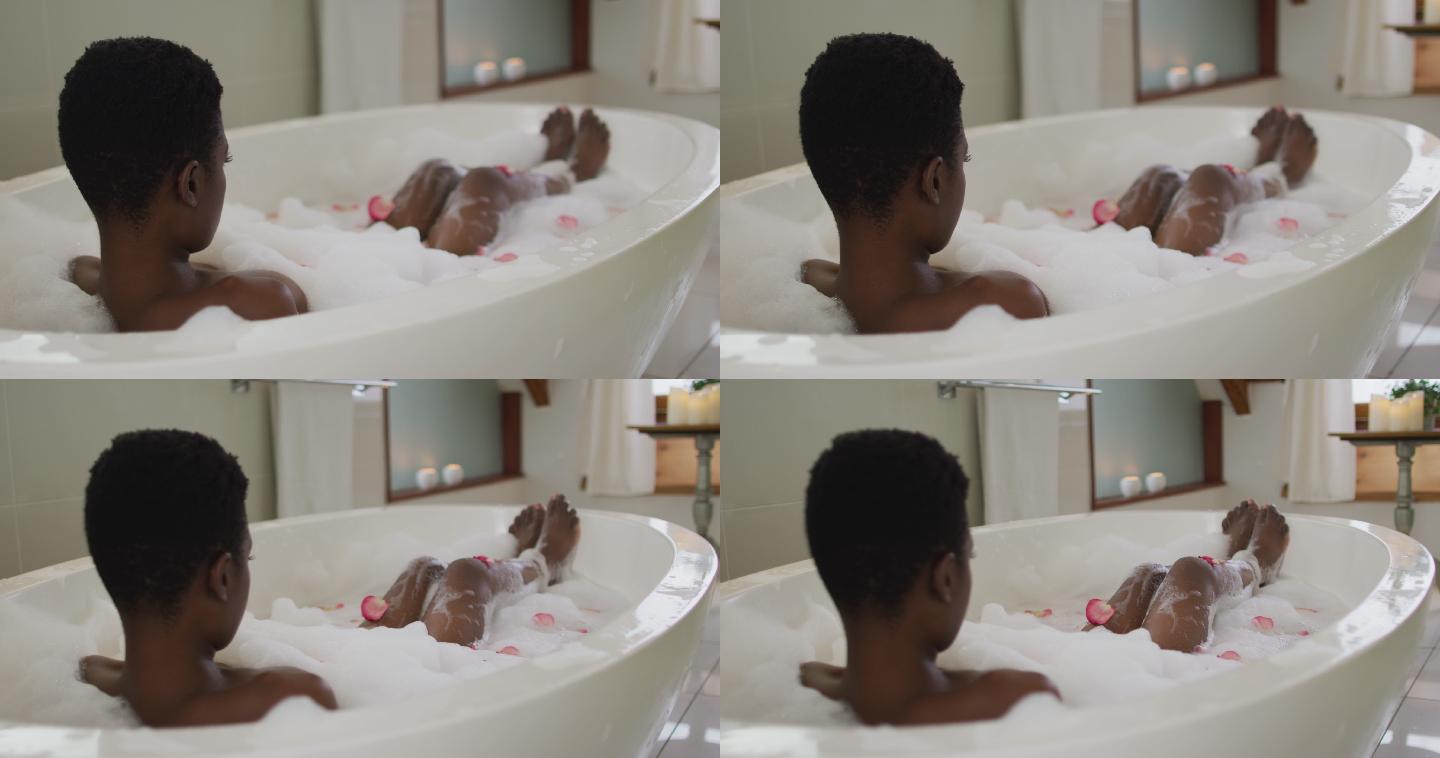 非洲裔美国人迷人的女人用泡沫和玫瑰花瓣洗澡的后视图