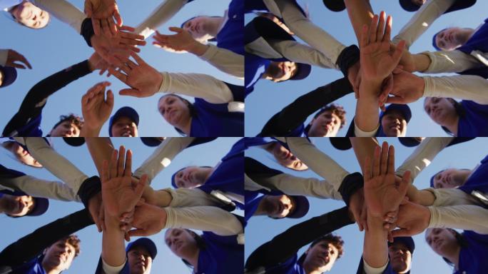 低角度的不同组女棒球运动员在蓝天下做手叠