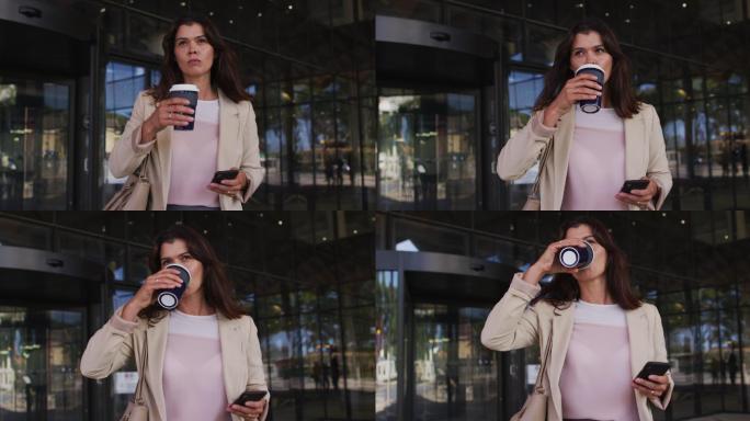 白人女商人在现代办公室外使用智能手机和喝外卖咖啡