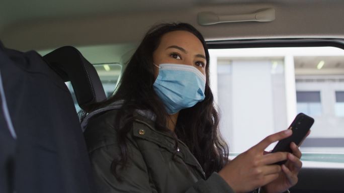 戴着口罩坐在车里使用智能手机的亚洲女性