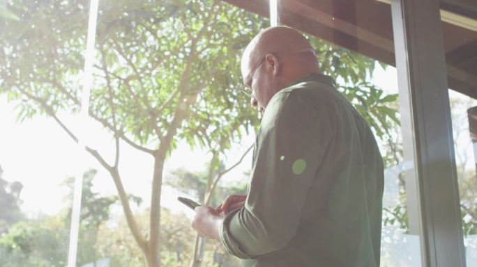 一位深思熟虑的非洲裔美国老人坐在阳台上晒太阳，用智能手机
