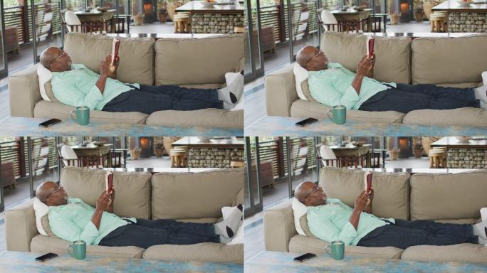 快乐的非裔美国老人放松，躺在沙发上看书