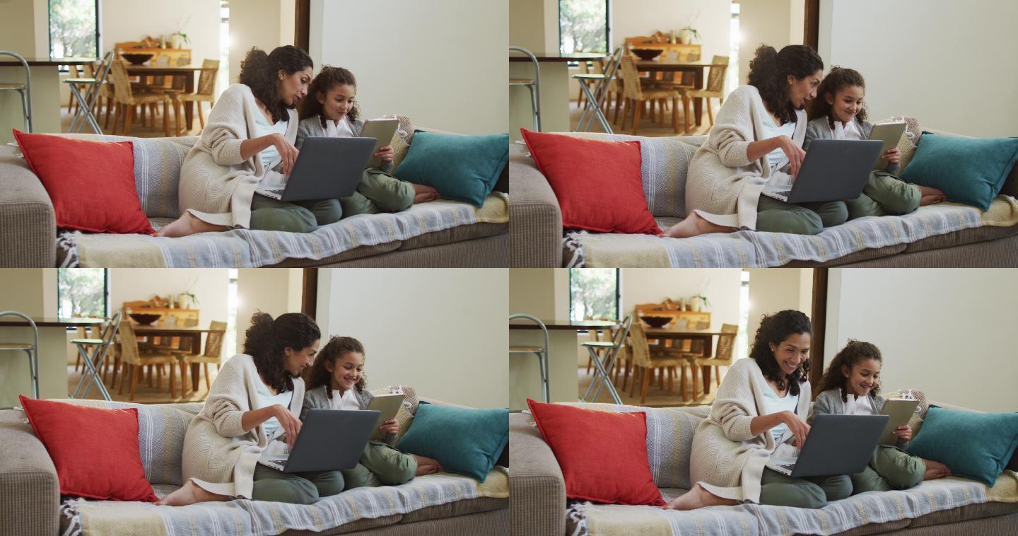 幸福的混血母亲和女儿坐在沙发上，玩得开心，并使用笔记本电脑