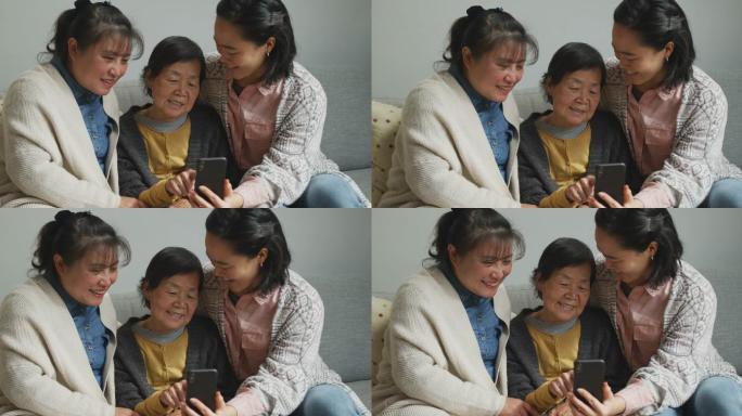 微笑着用智能手机与成年女儿和孙女拥抱的年长亚洲女性
