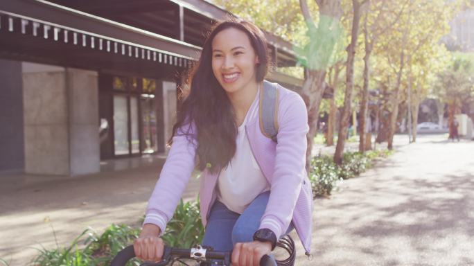 亚洲妇女背着双肩包微笑着骑自行车在路上