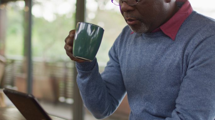 非裔美国老人坐在厨房柜台边吃药片，喝咖啡