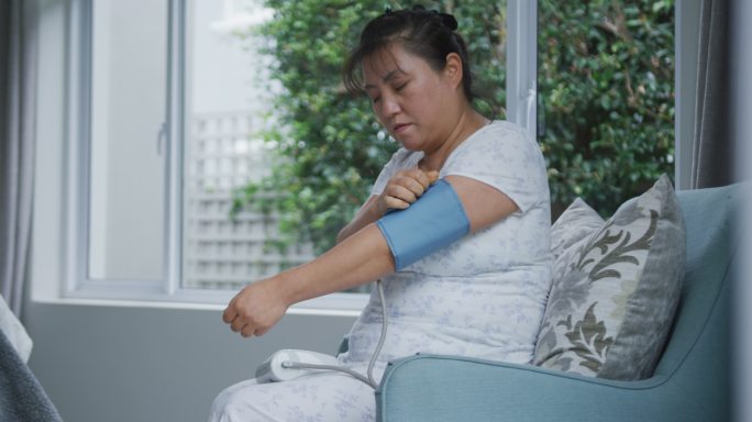 亚洲妇女使用血压监测器坐在家里的沙发上