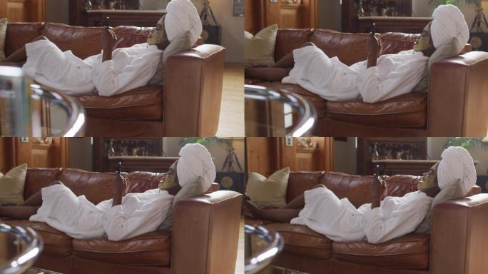 非裔美国美女戴着面膜躺在沙发上，在家里用智能手机