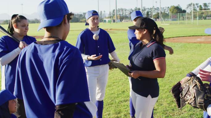 不同群体的女棒球运动员听着女教练在球场上用剪贴板说话