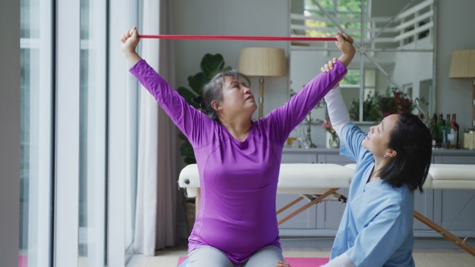 亚洲女性理疗师帮助女性患者在手术中用运动带锻炼手臂