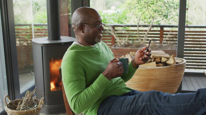 微笑的非洲裔美国老人放松的双脚，使用智能手机和喝咖啡