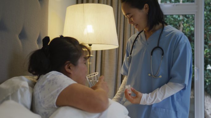 微笑的亚洲女医生帮助女病人在床上吃药