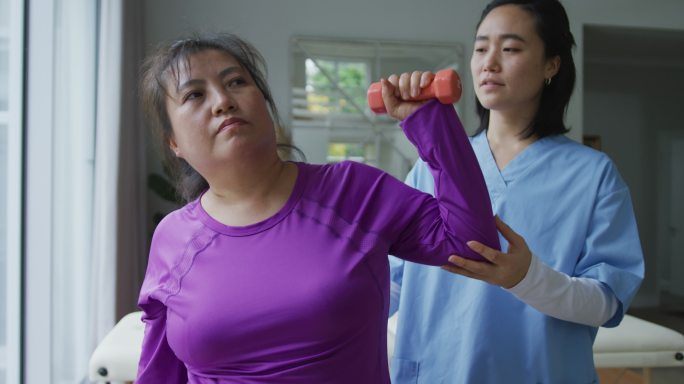 亚洲女性理疗师帮助女性病人在手术中用哑铃锻炼手臂