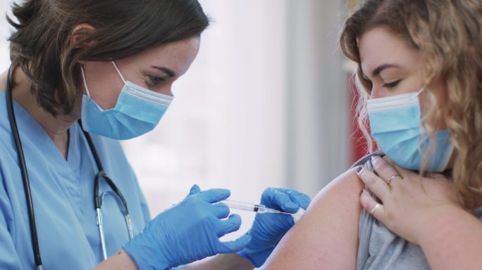 白种人女性和白种人女医生在家戴着口罩接种疫苗