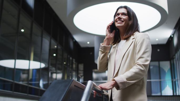 微笑的白人女商人在现代办公室大厅使用智能手机