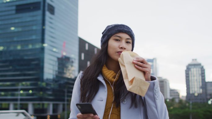 亚洲女性走路用手机吃三明治