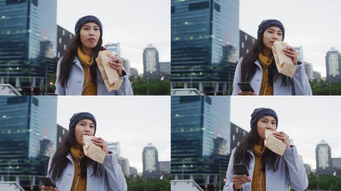 亚洲女性走路用手机吃三明治