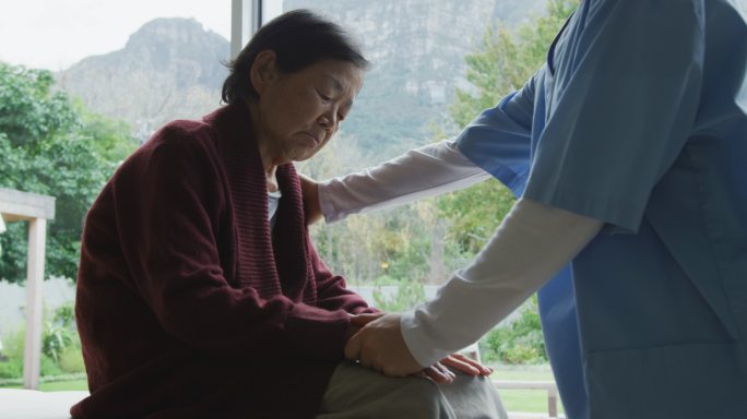 微笑的亚洲女医生安慰资深女病人，并在手术交谈