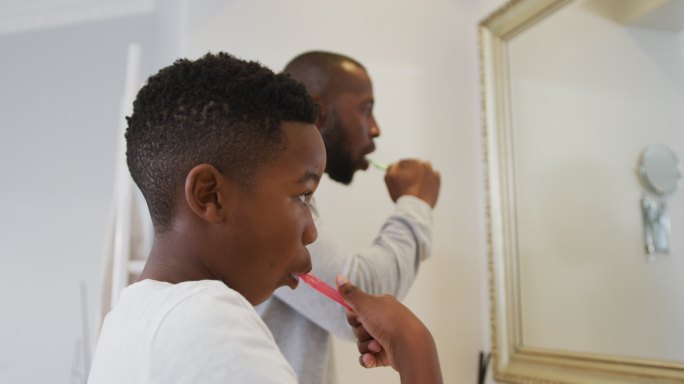 非裔美国人爸爸和儿子在家一起刷牙，看着镜子