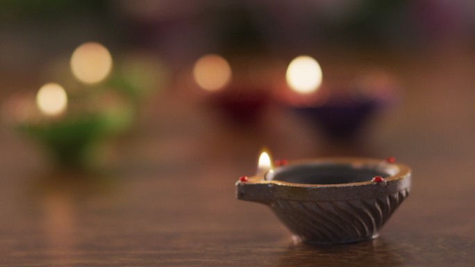 在木制桌面的装饰陶罐中点燃蜡烛，把焦点放在前景一处，散景背景
